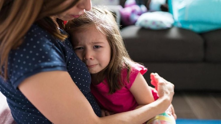 Mother consoling crying adorable girl while sitting in living room at home