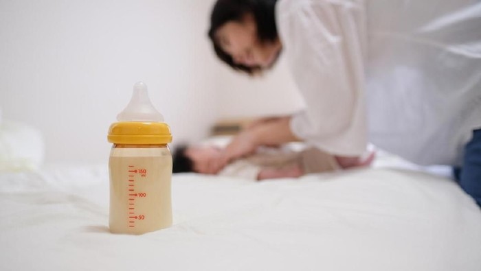 woman pouring milk in to bottles for new baby on wooden table