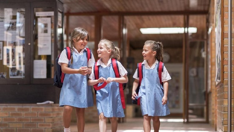 Full length of girls leaving from school. Cute carefree students are wearing school uniforms. They are carrying backpacks while walking together.