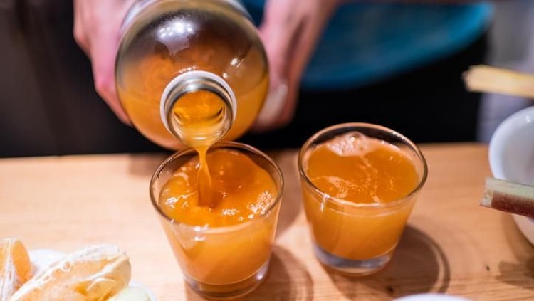 kunyit asam Woman person serving pouring kombucha fermented tea into two juice shot glasses on wooden table from bottle