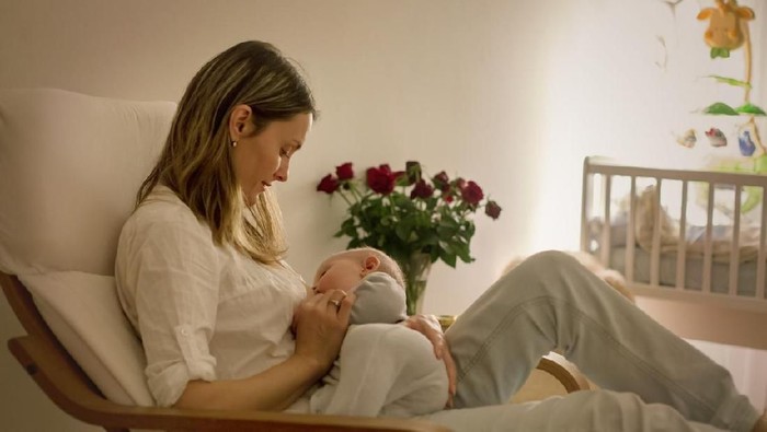 Young beautiful mother, breastfeeding her newborn baby boy at night, dim light. Mom breastfeeding infant