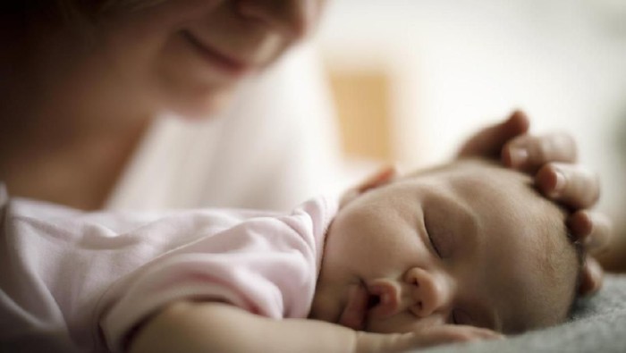 Young beautiful mother, breastfeeding her newborn baby boy at night, dim light. Mom breastfeeding infant