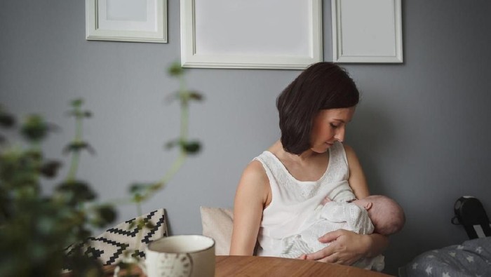 Young beautiful mother, breastfeeding her newborn baby boy at night, dim light. Mom breastfeeding infant