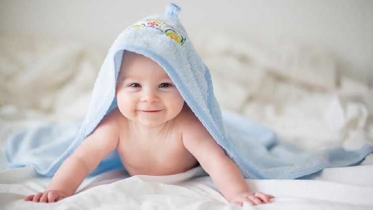 Cute little baby boy, relaxing in bed after bath, smiling happily, daytime