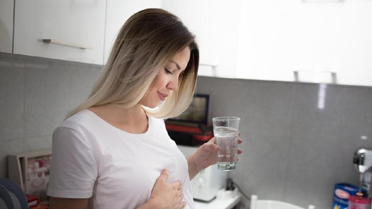 Unrecognizable pregnant lady massaging breast suffering from pain and discomfort sitting on couch at home. Cropped