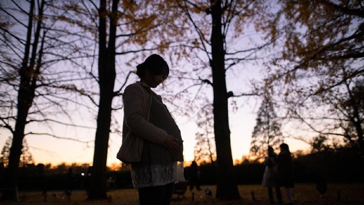 Silhouette of pregnant woman holding her abdomen in twilight