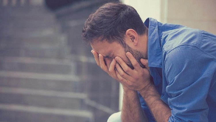 side profile stressed sad young crying man sitting outside holding head with hands looking down. Human emotion feelings