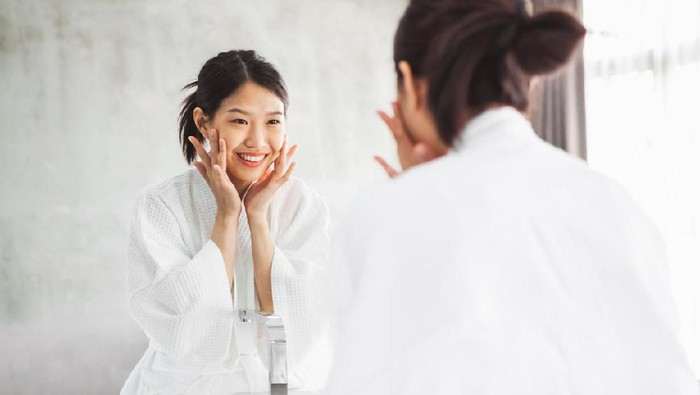 Asian woman cleaning face front of mirror, skin care and cosmetic removal concept