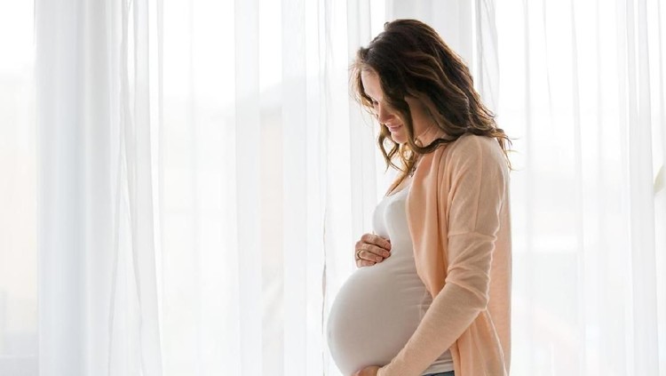 Portrait of young pregnant attractive woman, standing by the window, dressed in casual clothing, day before due date