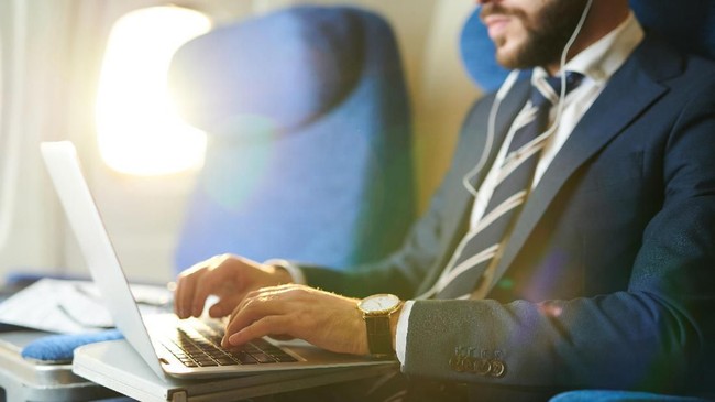 Mid section portrait of unrecognizable businessman typing on keyboard while using laptop during first class flight in plane, copy space