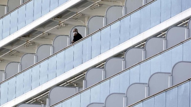 A passenger stand outside on the balcony of the cruise ship Diamond Princess anchored at the Yokohama Port Thursday, Feb. 6, 2020, in Yokohama, near Tokyo. The 3,700 people on board faced a two-week quarantine in their cabins. Health workers said 10 more people from the Diamond Princess were confirmed sickened with the virus, in addition to 10 others who tested positive on Wednesday. The 10 will be dropped off as the ship docks and transferred to nearby hospitals for further test and treatment. (AP Photo/Eugene Hoshiko)