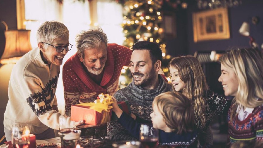 Happy senior grandparents giving Christmas presents to their family in dining room.