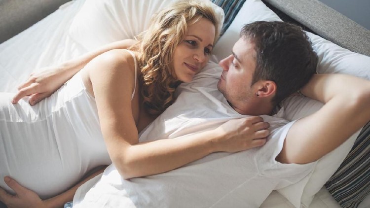 Pregnant happy wife lying in bed with husband