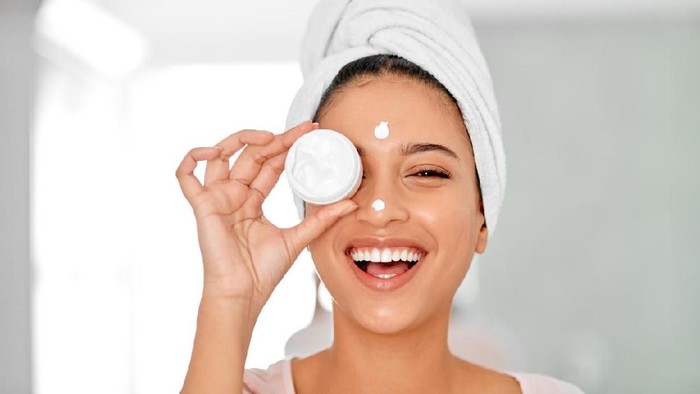 Shot of an attractive young woman covering her eye with a beauty product in her bathroom at home