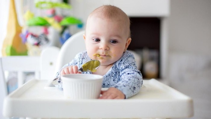 Cute little baby boy, eating mashed vegetables for lunch, mom feeding him, sweet toddler boy, smiling