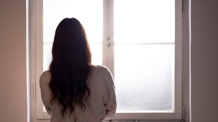 Woman suffering from cancer looking through hospital window.