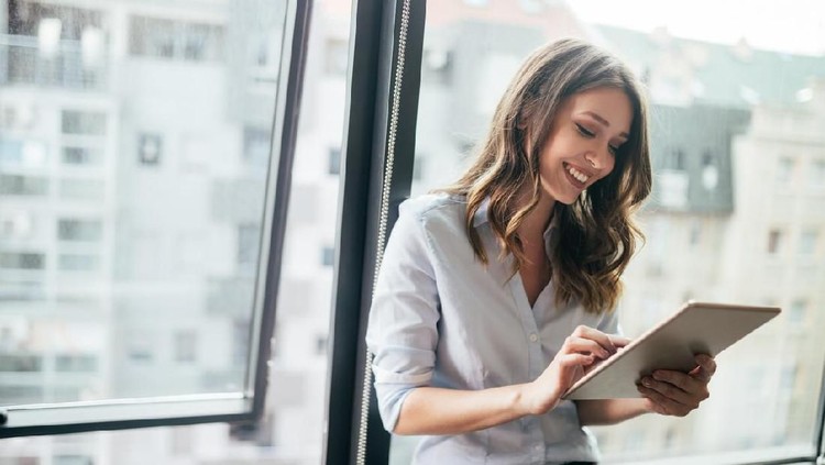 zodiak Young businesswoman using a digital tablet while standing in front of windows in office