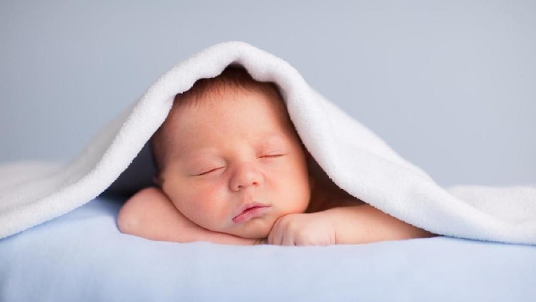 Color photo of a newborn baby boy sleeping peacefully under a soft blanket.