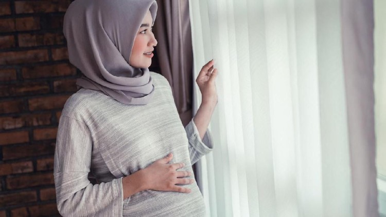 Expecting muslim woman stroking belly sitting on sofa, carrying child harmony