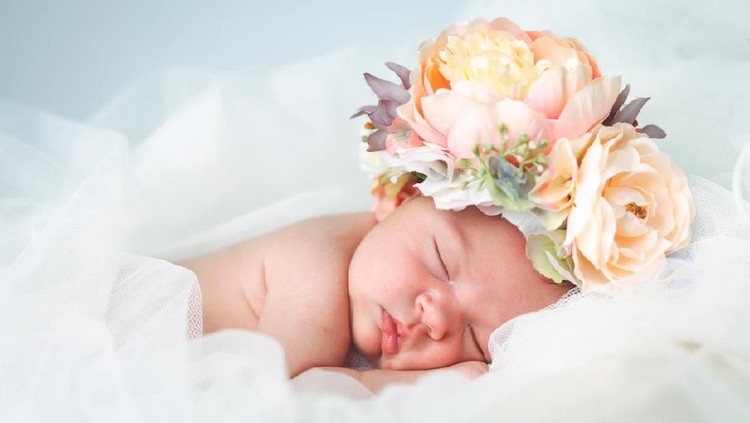 679510070 A newborn baby girl, fast asleep, wears a bonnet of flowers.
