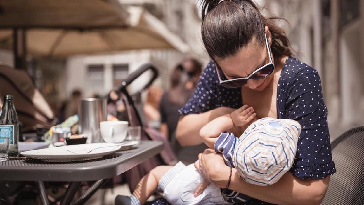 Young mother breastfeeding her baby boy in public place. Trieste, Italy, Europe