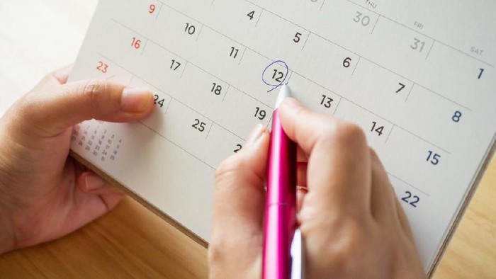 Young woman hand holding red clock Ovulation test strip with calendar in background. Positive result. It is a time for baby.Gynecology concept