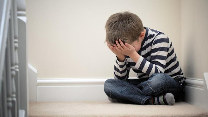 Upset problem child with head in hands sitting on staircase concept for childhood bullying, depression stress or frustration