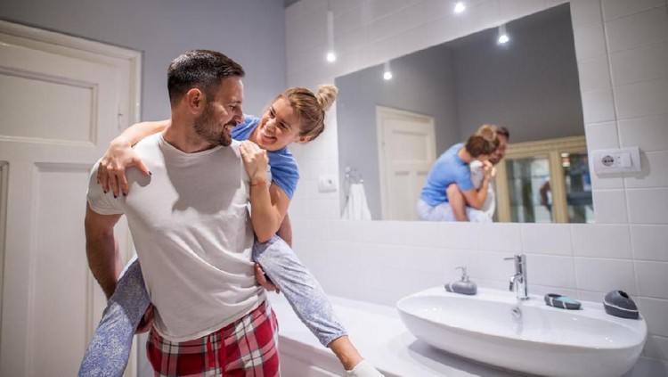 Cropped shot of an attractive young woman using toothpaste while her husband embraces her in their bathroom at home