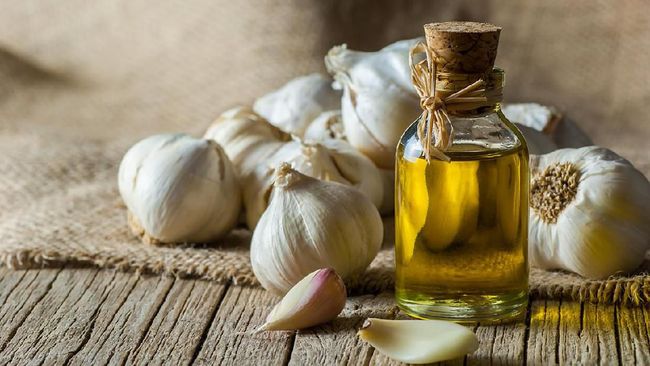 Ripe and raw garlic and garlic oil in glass of bottle on wooden table with burlap sack, alternative medicine, organic cleaner. Garlics background
