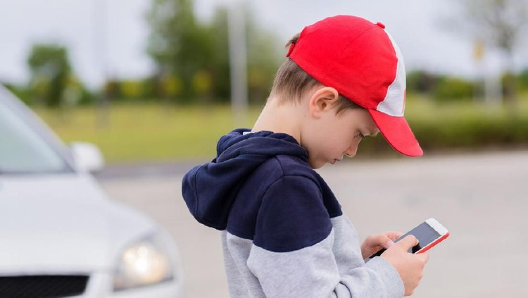 Anak main gadget Child busy playing the smartphone mobile games does not pay attention to the moving car. Boy child playing mobile games on smartphone on the street