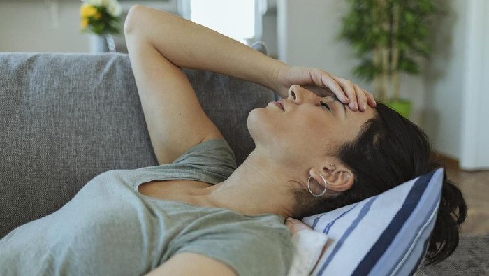 Unhappy Woman Touching Her Head and Suffering From Headache. Portrait of an Attractive Young Woman Sitting on a Sofa at Home With a Headache, Feeling Pain and With an Expression of Being Unwell. People, Emotions, Stress and Health Care Concept