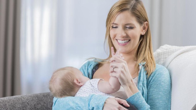 Confident female pediatrician examines a newborn baby. The baby's mother is holding her. The doctor is touching the baby's head. Baby bottles and a doctor's bag are on a table.