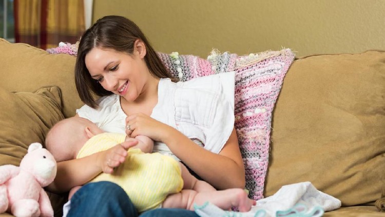 Confident female pediatrician examines a newborn baby. The baby's mother is holding her. The doctor is touching the baby's head. Baby bottles and a doctor's bag are on a table.