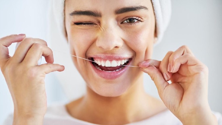Portrait of a beautiful young woman flossing her teeth in the bathroom at home