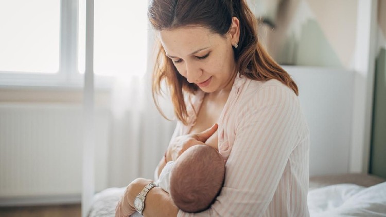 Portrait of a loving mother in sofa breastfeeding baby girl. Newborn child fed with breast milk by mom.
