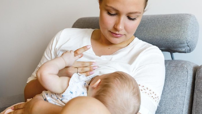 Portrait of a loving mother in sofa breastfeeding baby girl. Newborn child fed with breast milk by mom.