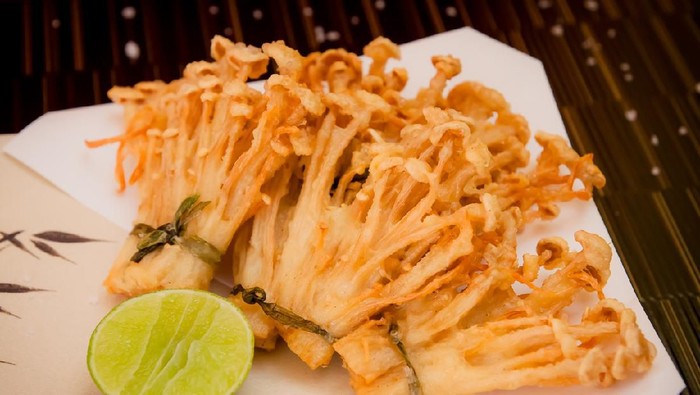 deep fried golden brown crispy Japanese enokitake needle shape mushroom with lime on black background