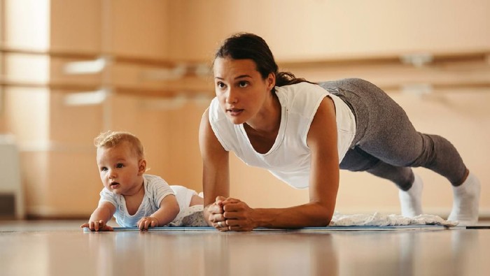Athletic mother exercising in plank position while being with her baby in a health club. Copy space.