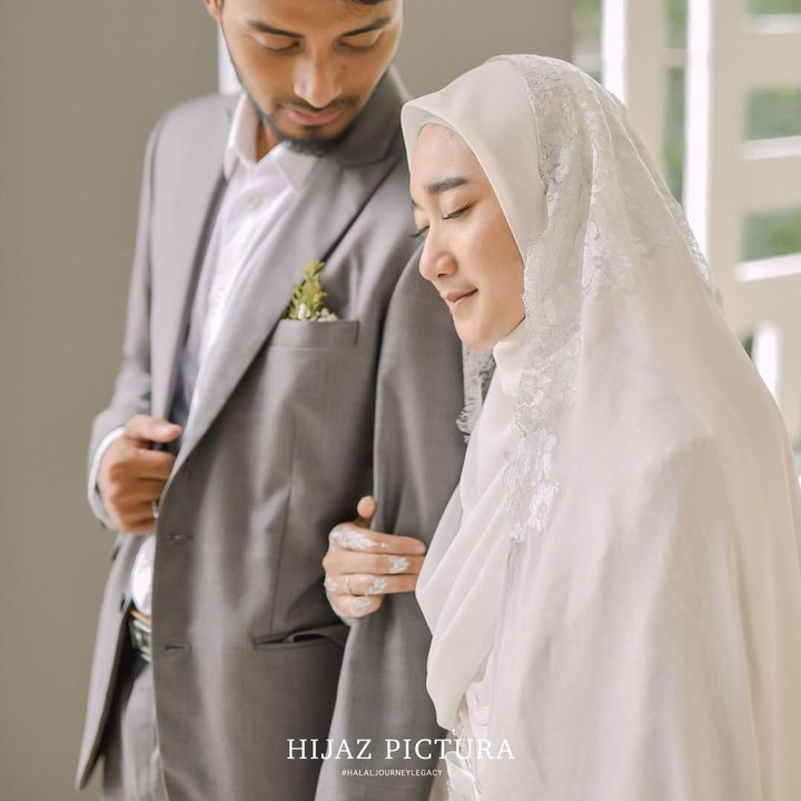 <p>Dena tampil cantik dibalut gaun putih, sedangkan Hawaariyyun rapih dengan setelan jas abu-abu dan kemeja putih. (Foto: Instagram @hijazpictura)</p>