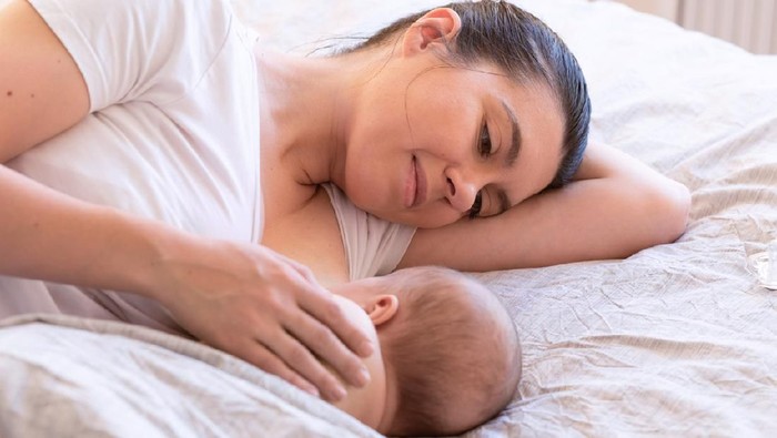 Close-up of mother breastfeeding and hugging newborn baby. Mom breast feeding her infant baby. Lactation newborn concept. Baby eating milk before sleeping. Mother feed her month son with breast milk