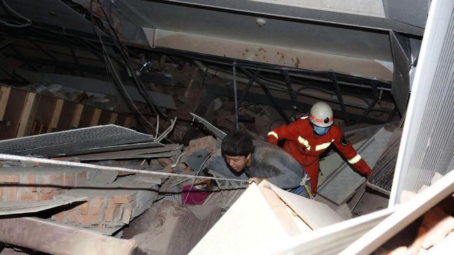 Seorang pria dibantu keluar dari puing sisa reruntuhan hotel di Quanzhou, China. Hotel yang digunaklan untuk karantina virus corona tersebut ambruk Sabtu (7/3). (Chinatopix via AP).