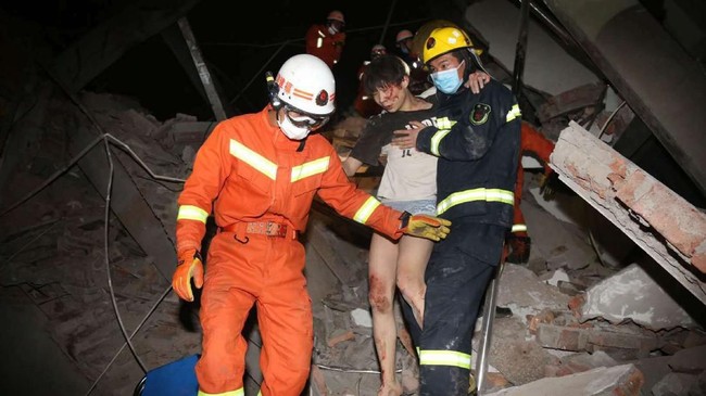 Tim penyelamat membantu seorang wanita yang terjaebak dalam reruntuhan hotel di Quanzhoue, China. Hotel yang digunakan sebagai lokasi karantina tersebut ambruk Sabtu (7/3) dan menimpa puluhan orang. (Chinatopix via AP).