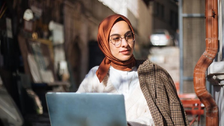 Young woman sitting at sidewalk cafe and using Laptop