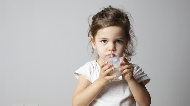 Caucasian toddler girl is drinking milk in studio.