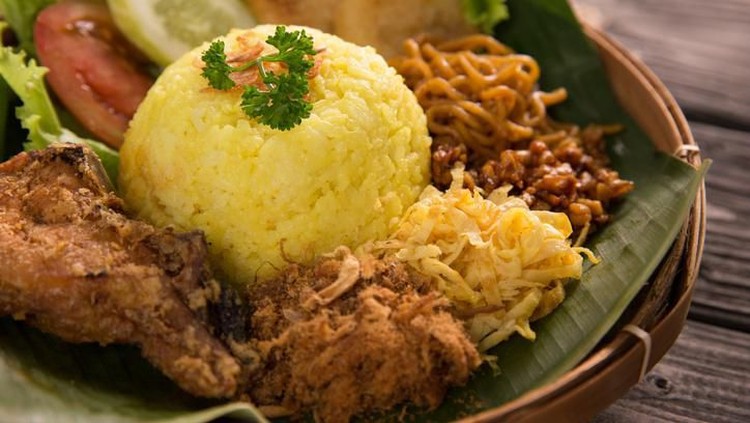 nasi kuning. indonesian yellow rice served with fried chicken on banana leaf