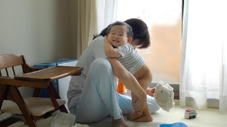 A smiling baby whose mother is changing a diaper