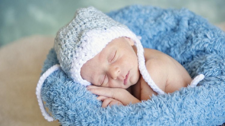 A sleeping preemie newborn baby boy wearing a hat, studio shot, focus on face