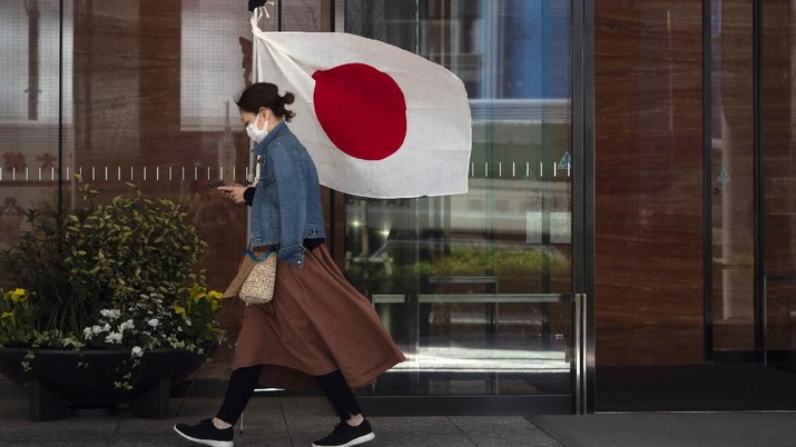A woman wearing a mask walks past a Japanese flag Wednesday, March 11, 2020, in Tokyo. For most people, the new coronavirus causes only mild or moderate symptoms, such as fever and cough. For some, especially older adults and people with existing health problems, it can cause more severe illness, including pneumonia. The vast majority of people recover from the new virus. (AP Photo/Jae C. Hong)