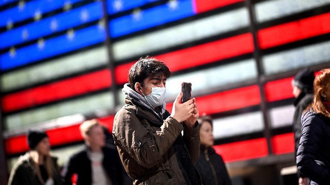 A man wears a mask as uses his cellphone at Times Square in front of an American flag on March 5, 2020  in New York City. (Photo by Johannes EISELE / AFP)