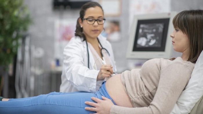 A pregnant woman and her female doctor are indoors in a hospital. The doctor is performing an ultrasound.